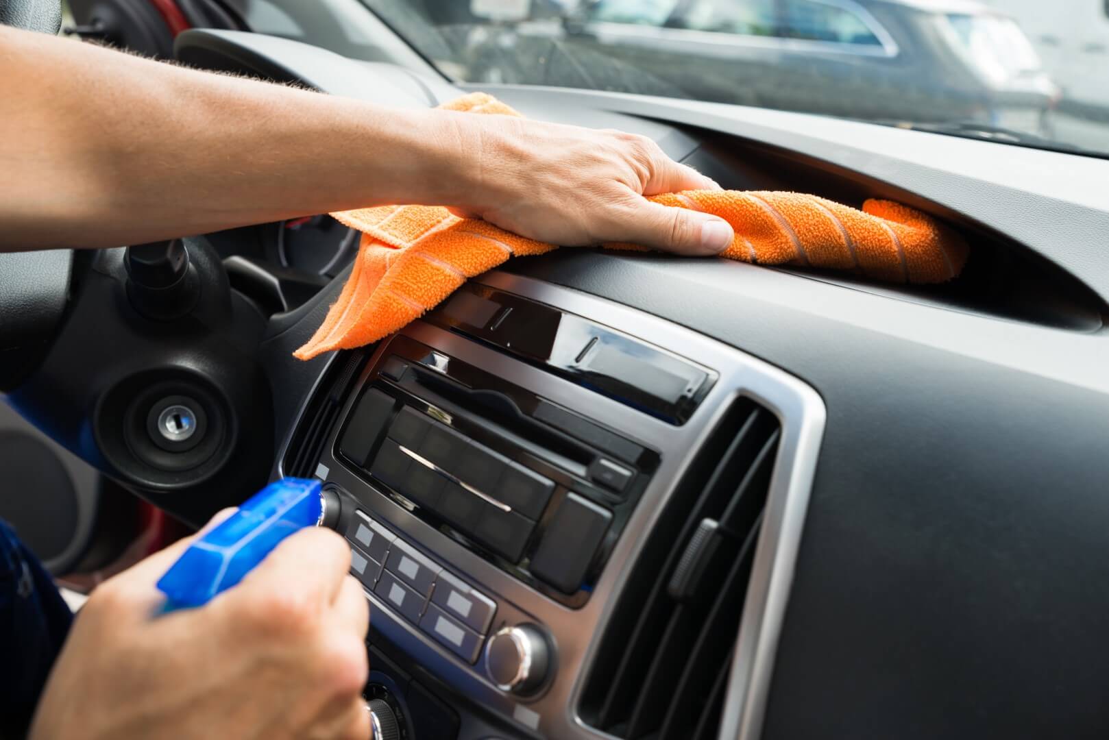 Image depicts a car detailing expert cleaning the dashboard of a car.